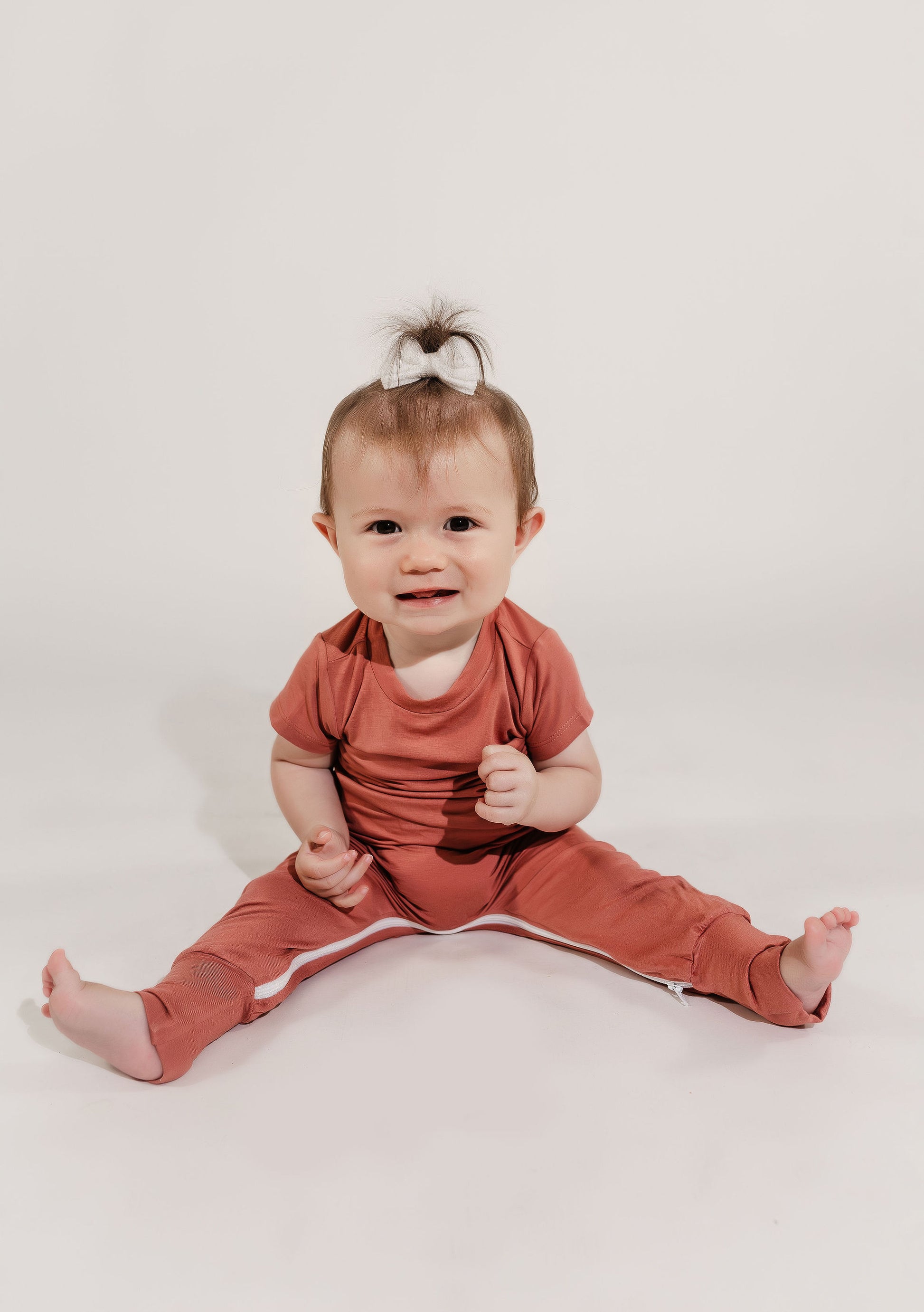 Baby wearing a red pink mauve outfit sitting on a white background wearing a Bamboo Lyocell Zipease Romper