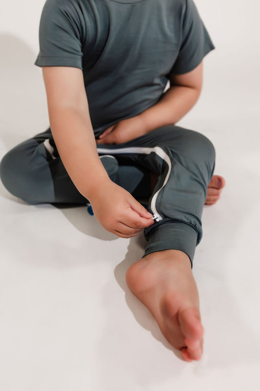 Little boy playing with his ankle to ankle zipper on his deep teal Bamboo Lyocell Zipease Romper