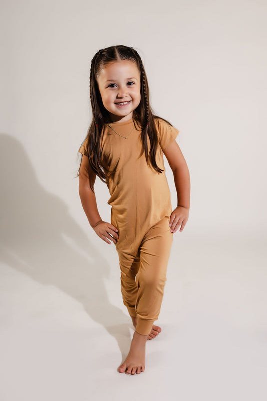 little girl with her hands on her hips smiling wearing a camel tan Bamboo Lyocell Zipease Romper