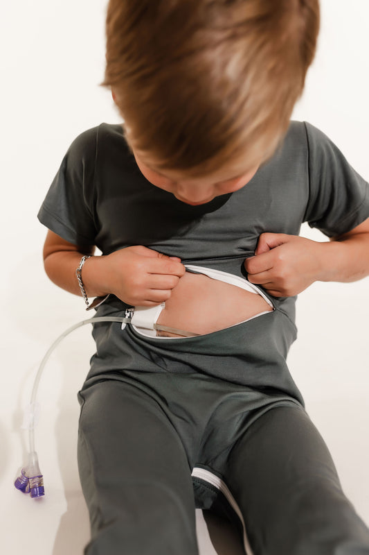 Child wearing a medical device on their abdomen against a white background wearing a Bamboo Lyocell Zipease Romper teal blue green gastrostomy tube gtube g-tube