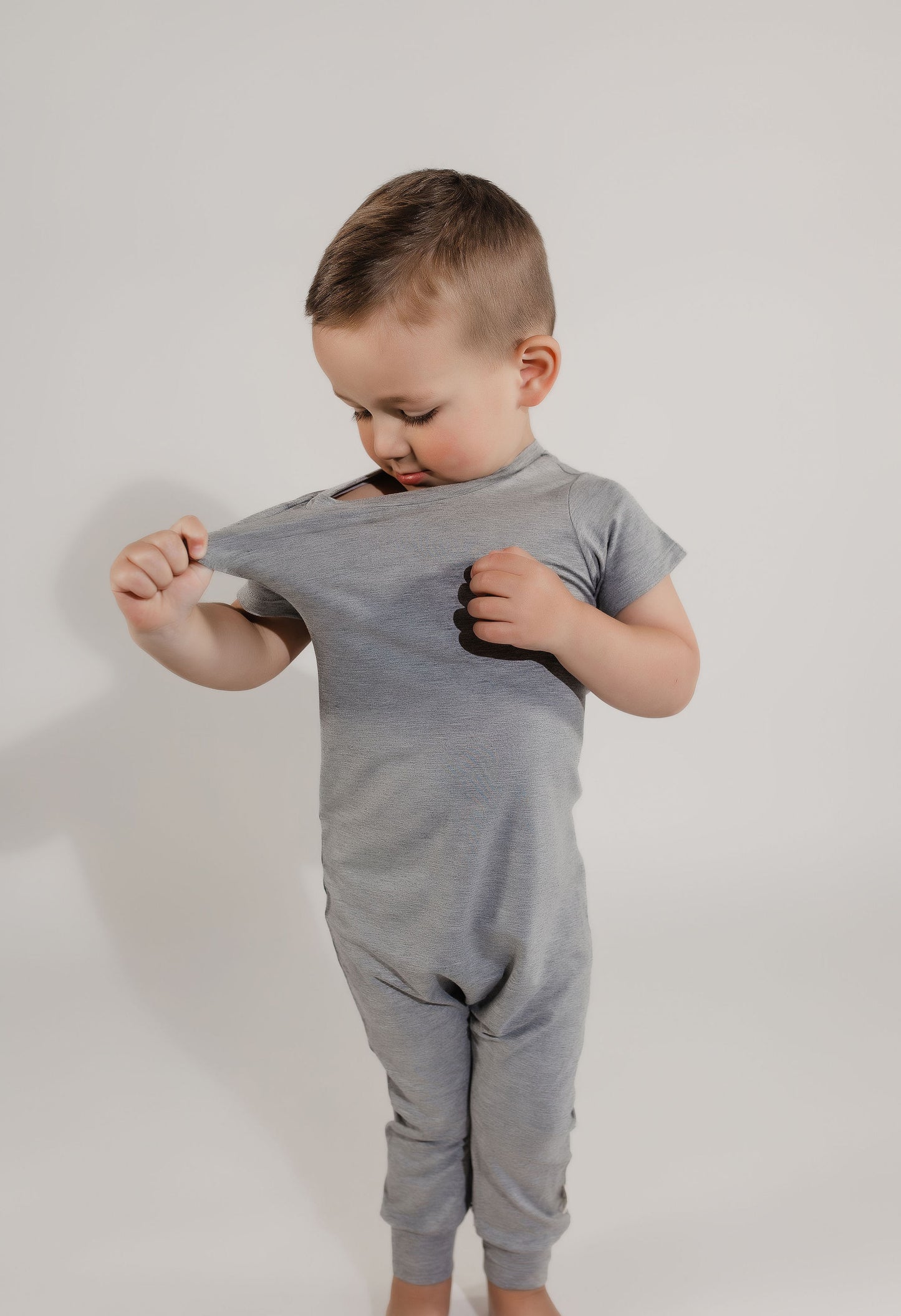 Little boy pulling on his stretchy neckband wearing a grey Bamboo Lyocell Zipease Romper