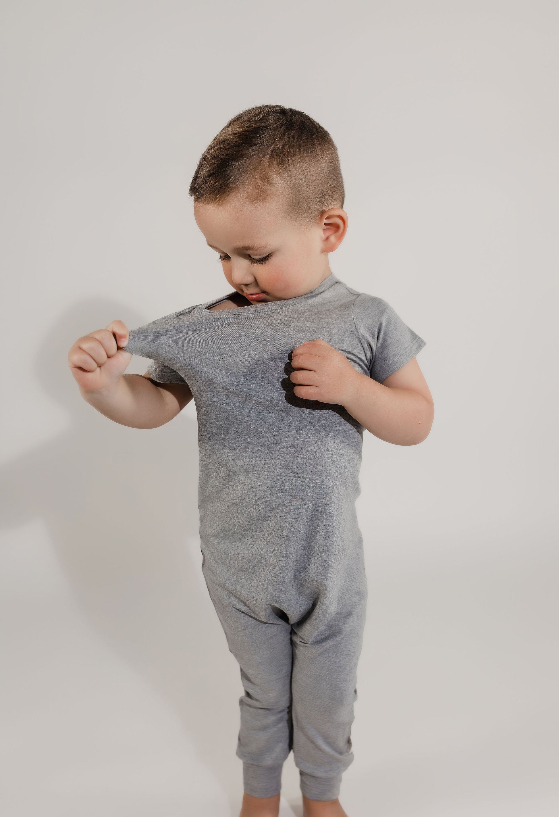 Little boy pulling on his stretchy neckband wearing a grey Bamboo Lyocell Zipease Romper