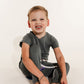 Child sitting on a white floor wearing a gray t-shirt and dark pants wearing a Bamboo Lyocell Zipease Romper g-tube gtube gastrostomy tube